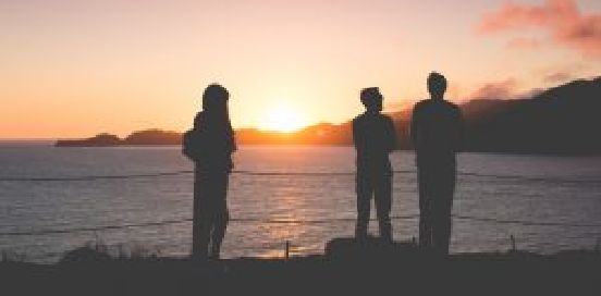three people standing by lake watching sunset