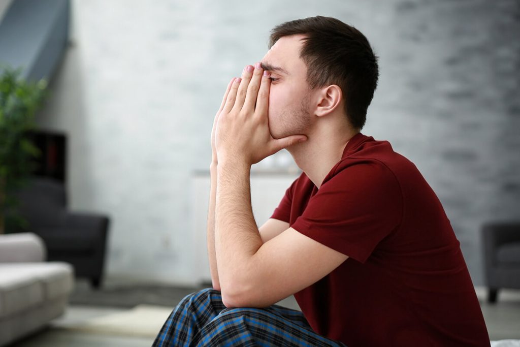 A man sits with his hands covering his mouth and nose, appearing tense and anxious, representing symptoms of a panic or anxiety attack.