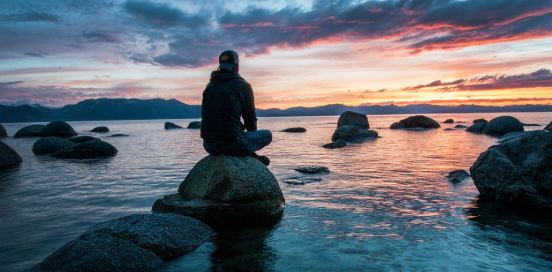 man sitting on a rock looking at the ocean