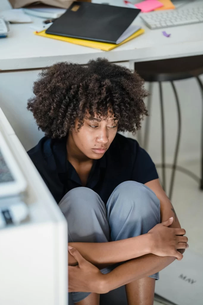 A woman sits on the floor with her knees pulled to her chest, appearing distressed and withdrawn, representing symptoms of post-traumatic stress disorder (PTSD)