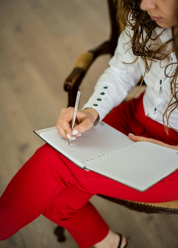 woman in white long-sleeve shirt writing on white paper